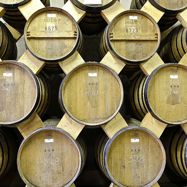 Des fût en bois empilés dans un entrepôt, utilisés pour le vieillissement de boissons alcoolisées.
