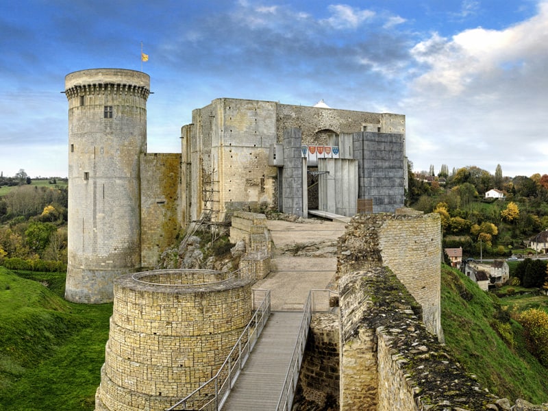 Vue du château de Falaise, avec une tour circulaire et des murs en pierre, surplombant un paysage vallonné.