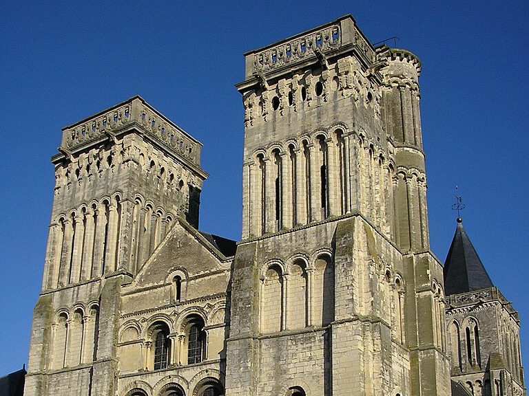 Abbaye romane, l'Abbaye aux Dames avec deux tours, façade sculptée, située sous un ciel bleu.