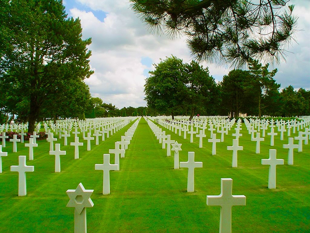 Cimetière militaire de Colleville avec des croix blanches et une étoile de David sur un terrain bien entretenu sous un ciel nuageux.