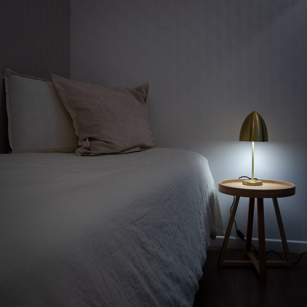 Chambre standard, moderne avec lit, coussins et lampe dorée sur table en bois. Ambiance douce et confortable.