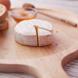 Plateau en bois avec fromage, pain, œuf et miel.