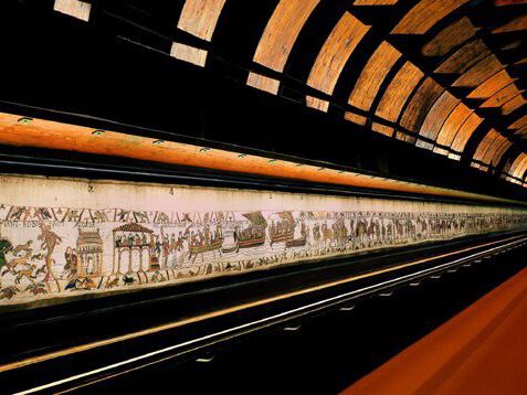 Tapisserie de Bayeux. Mural historique illustrant des scènes médiévales, situé dans un cadre moderne et soigné.
