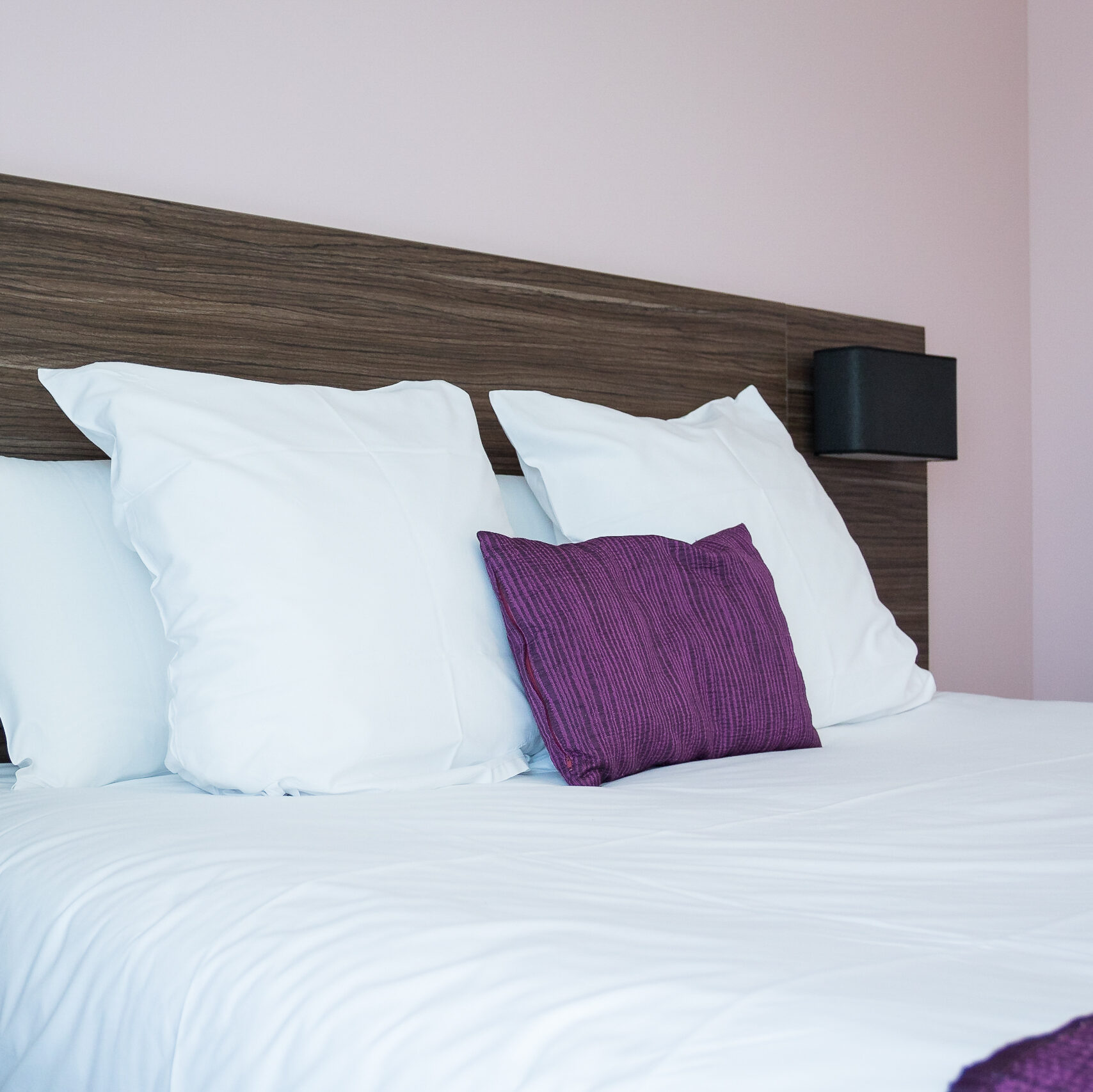 Lit confortable avec oreillers blancs et coussin violet dans une chambre standard de l'Hôtel Libéra à Colombelles.
