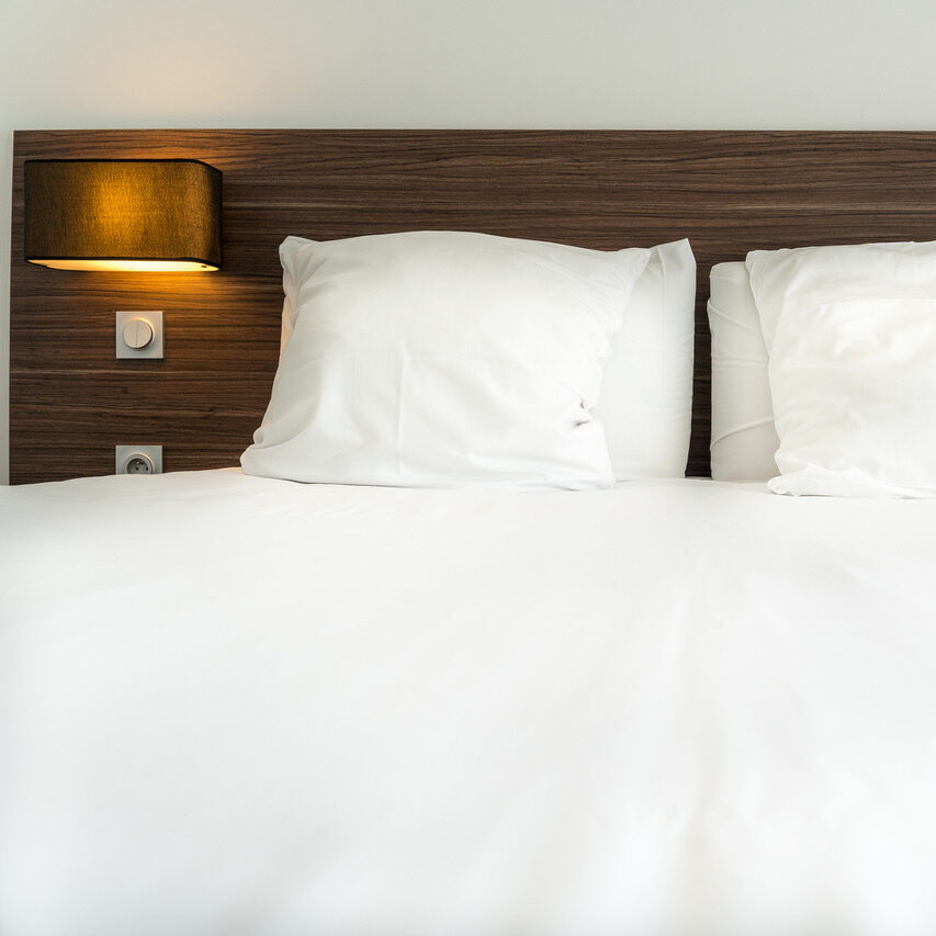 Lit confortable avec oreillers blancs et lampe sur tête de lit en bois dans une chambre d'hôtel Studio moderne.