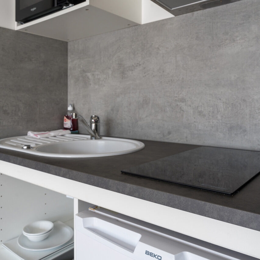 Cuisine moderne et épurée d'une chambre studio de l'hôtel Libéra, avec évier, plaque de cuisson et espace de rangement.