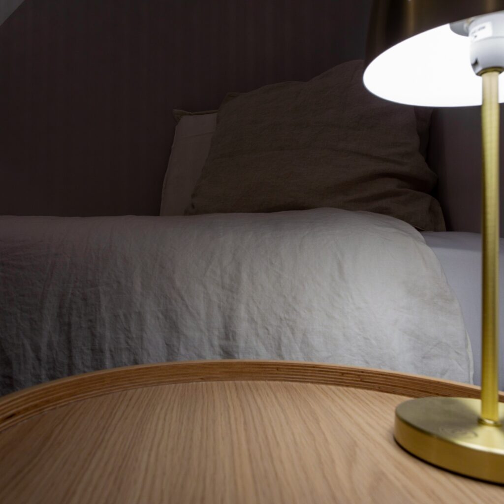 Coin d'une chambre standard, moderne avec un lit, un coussin et une lampe de table sur une table en bois.